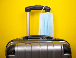Suitcase with protective masks on yellow background