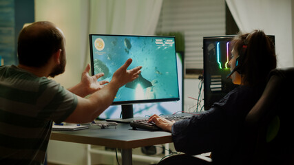 Fototapeta premium Excited couple players wining space shooter video game during virtual competition tournament using professional headset. Excited online streaming cybers performing gaming using RGB powerful computer