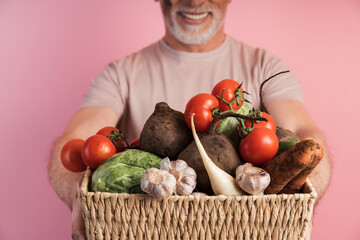 Close view, basket with vegetables, man holding fresh vegetables. Isolated on pink background,...
