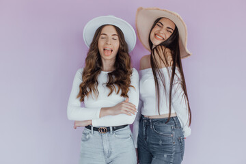 Picture of excited two ladies friends standing isolated over pink background. 