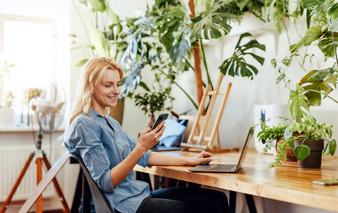 Young female office worker with a smartphone and laptop in office