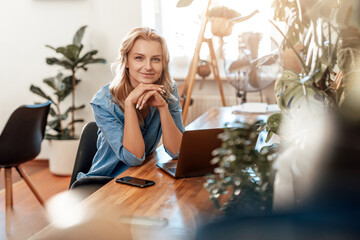 Thoughtful young woman poses in office room with laptop at table