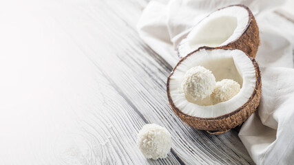 Two halves of coconut and coconut sweets on a wooden table .  Coconuts on a white napkin . Handmade coconut sweets with a copy space  .  Horizontal orientation picture with a coconut .