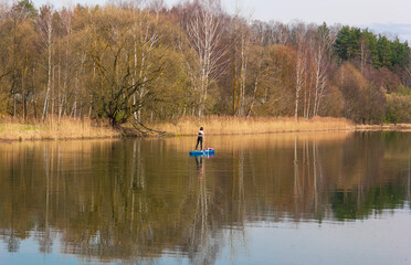 Fototapeta na wymiar Warm colors in early spring by the lake with a view of nature. Lonely girl on a canoe goes in for sports