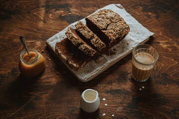 Chocolate banana bread on a wooden cutting board and a linen napkin, a glass of coffee with cream,...