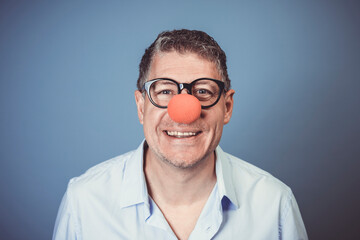 business man with blue shirt and black glasses and red clown nose posing in front of blue background in the studio