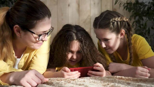 Happy family. Family watching videos on smartphone. Happy family is watching video on smartphone. Happy children with mom lie on bed. Family teamwork. Children smile while watching video on smartphone