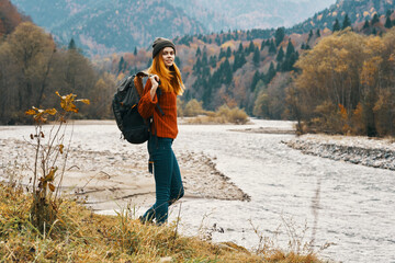 woman in jeans and a jacket with a backpack near the river in the mountains landscape nature