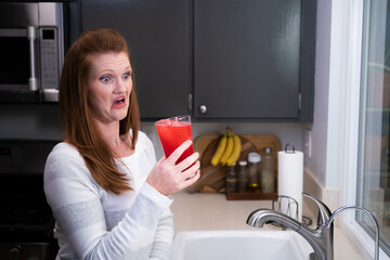 Red Head Caucasian Woman Mother Mom in Kitchen Looking at Blended Red Health Drink Smelling Disgussting Gross Foul Ingredients Funny Face