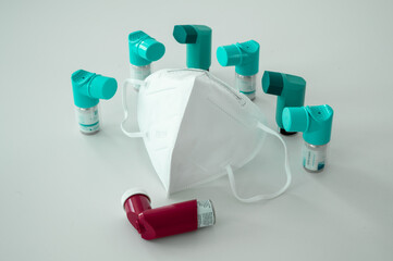 Various asthma spray inhalers and a Covid-19 respirator mask on a white surface	
