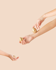 Young woman's and children's hands with gold Easter eggs on the pastel beige background with copy space. Minimal creative, festive, luxury concept.