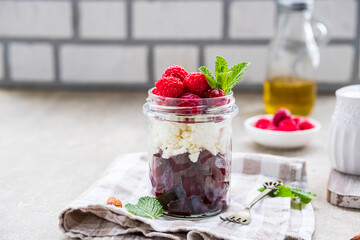 A healthy salad with beets, cream cheese or cottage cheese, nuts and raspberries in a glass jar on a light concrete background. Salad recipes.