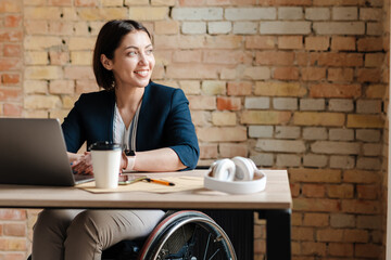 White smiling woman in wheelchair working with laptop at office