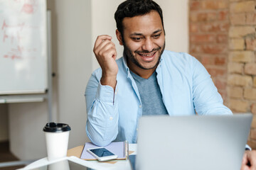 Middle eastern smiling man working with laptop while sitting at desk