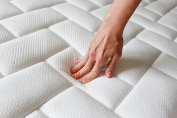 Cropped shot of young woman's hand testing white orthopedic mattress on firmness. Female pressing...