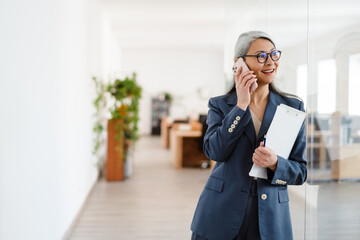 The happy Asian woman talking on the phone while looking to the side in a light office