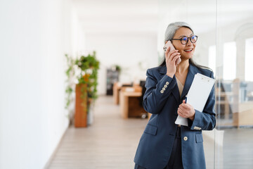 Fototapeta premium The happy Asian woman talking on the phone while looking to the side in a light office