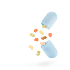Colorful jelly candies with vitamins and minerals fall out from the open pastel blue capsule isolated on white background. Minimalist supplement health care concept.