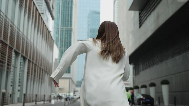 4k slow motion back view of one Young Asian businesswoman wearing a white suit running on the street surrounded by tall office buildings young people after freedom dream