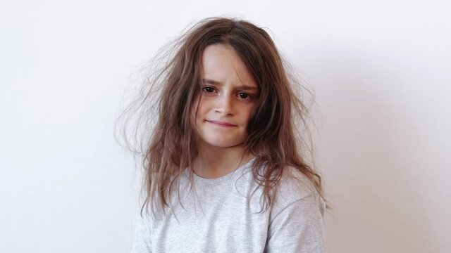 Child haircare. Beauty care. Hygiene cosmetology. Dissatisfied disappointed unhappy little girl with dry tousled tangled untidy messy hair isolated on light background.