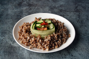 Buckwheat with a salad of tomatoes, cucumbers and dill with olive oil on a white plate. Vegetarianism. Lean food.