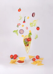 Food levitation. Taco with mixed vegetables: tomato, onion, pepper and lettuce. White background. Close up.