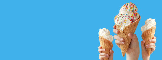Hands holding a vanilla ice cream cone on blue background. Banner.