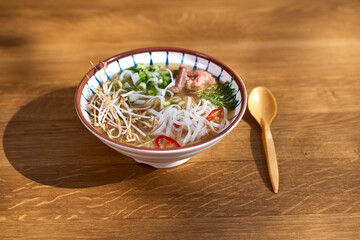 Asian pho bo soup, best pho broth, in a light bowl on a wooden table
