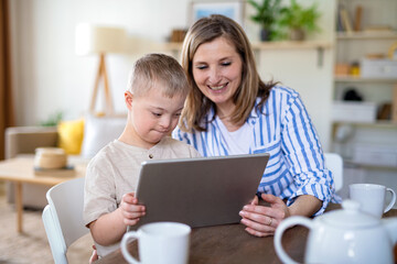 Single mother with down syndrome child at home, using tablet.