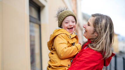 Single mother holding down syndrome child outdoors in town, laughing.