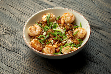 Delicious Asian street food - wok rice with shrimps, green onions, vegetables and sesame seeds in a white bowl on a wooden background.