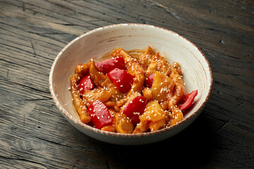 Delicious Asian street food - sweet and sour chicken with sesame seeds and bell pepper in a white bowl on a wooden background.