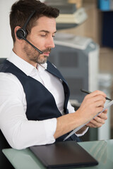 businessman wearing headset with microphone taking notes