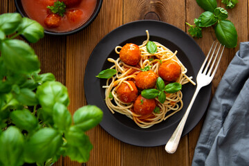 Spaghetti with eatballs tomato sauce , basil leaves in black mate plate on wooden background, delicious mediteranean food
