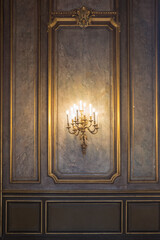un chandelier en forme de bougies de style contre un mur patinée de gris et des boiseries en or