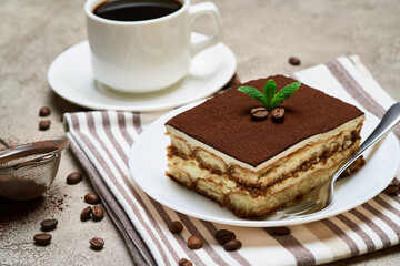 Portion of Traditional Italian Tiramisu dessert and cup of coffee on grey concrete background