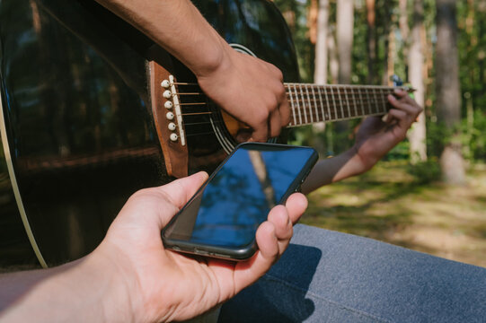 Close-up of a telephone in front of a man playing the guitar. Against the background of the forest. - Powered by Adobe