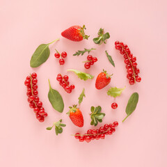 Circular shape made of strawberries, red currants berries and vegetable green leaves on pastel pink background. Summer fruit and greens flat lay. Minimal food concept.