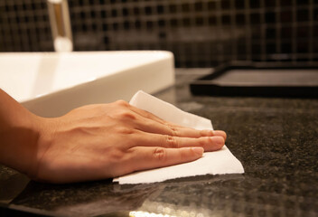 Cleaning surface. Closeup of hand using paper wipe cleaning dark stone marble surface. Concept of disinfection surface to prevent coronavirus infection, get rid of dust, germs. Selective focus.