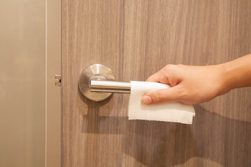 Closeup of hand opening the public doorknob with tissue paper. Concept of prevent spreading of coronavirus infection.