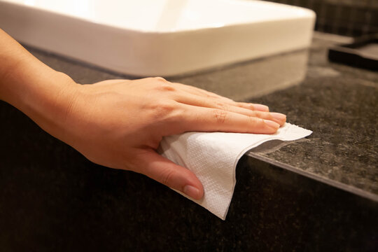 Cleaning Surface. Closeup Of Hand Using Paper Wipe Cleaning Black Marble Restroom Counter Surface. Concept Of Disinfection Surface To Prevent Coronavirus, Dust And Germs. Selective Focus