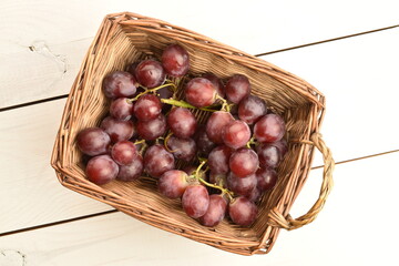 A bunch of fresh organic, juicy, ripe, sweet grapes in a wicker basket, close-up, on a painted table made of wood. Another bunch of grapes lies on the table.