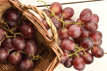 A bunch of fresh organic, juicy, ripe, sweet grapes in a wicker basket, close-up, on a painted table made of wood. Another bunch of grapes lies on the table.