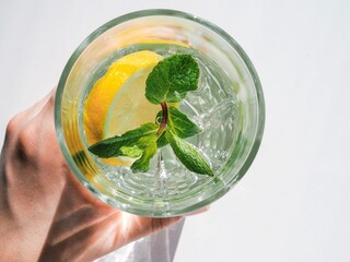 Woman's hand holding glass of water, lemon and mint. Wellness, healthy food, drinks, diet, detox. Summer drink Lemonade