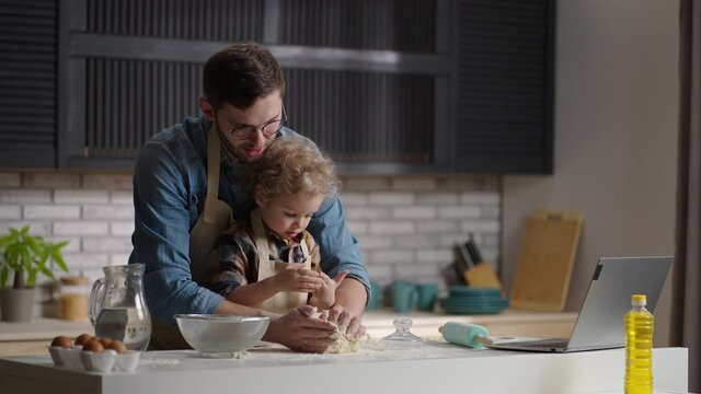 little boy and his father are cooking bread together at home, kneading dough on table kitchen, medium portrait
