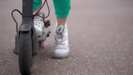 Close up low angle view 4K stock video footage of woman riding black electric kick scooter in streets of city on spring day