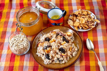 Oatmeal porridge, honey, dried apple, plums and butter on colorful table-cloth.