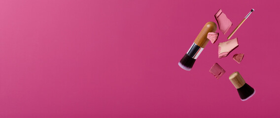 Obraz premium Flying makeup brushes and pieces of decorative cosmetic against pink background.Banner for beauty ad