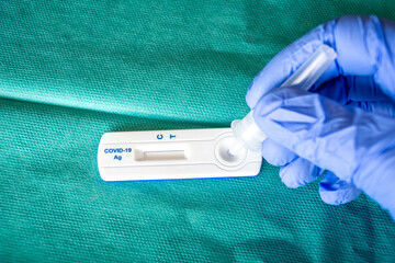Close up of health care worker wearing blue surgical gloves and placing the sample in the covid-19 antigen diagnostic drug on a green surgical fabric 