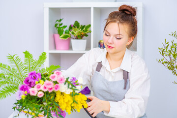 Cute girl florist collects a bouquet in a flower shop. A beautiful florist creates a composition of flowers. Girl cuts flowers and removes stale leaves.